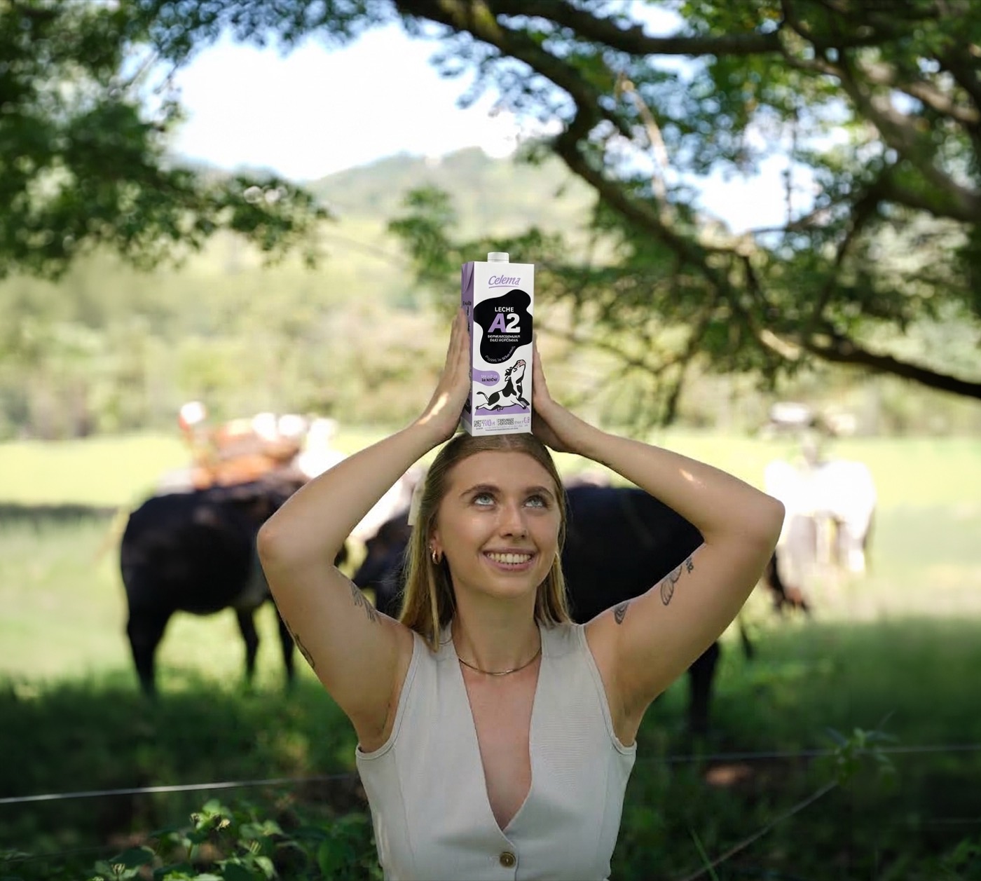 Ganadera con un empaque de Leche Celema A2 sobre la cabeza, con vacas pastando al fondo