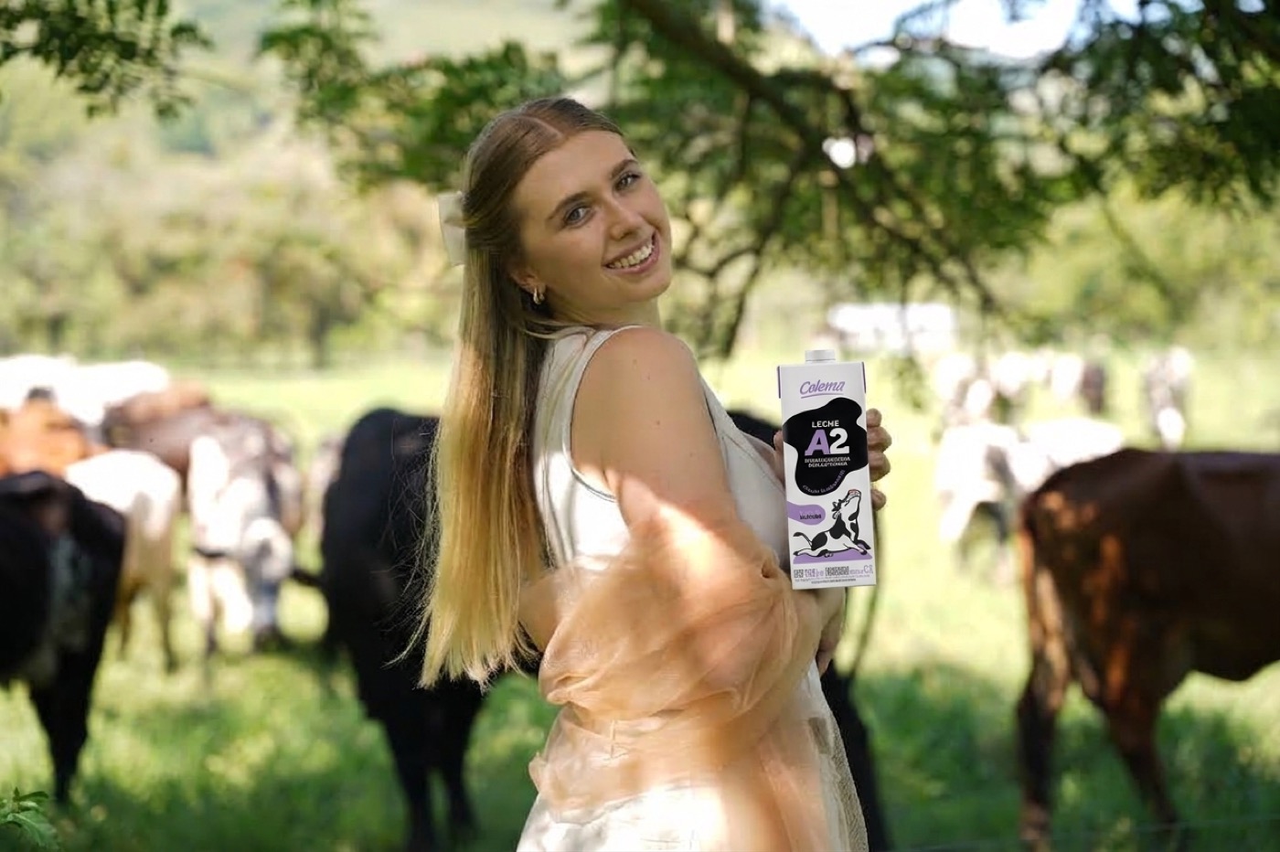 Ganadera sonriente con un empaque de Leche Celema A2 en medio del hato